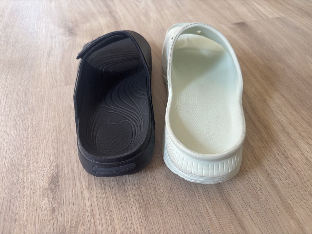 Rear view of black VALSOLE and white HOKA recovery slides.
